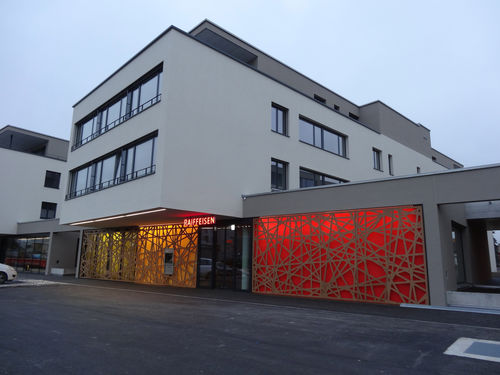 Exterior fitting decorative panel - RAIFFEISEN BANK HEIMBERG - Bruag Design Factory AG - wall-mounted / backlit / HPL