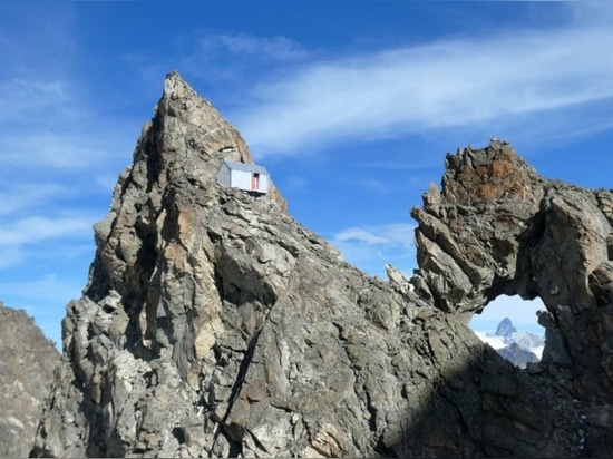 A bivouac is lightly perched on a rocky peak of the Italian Alps