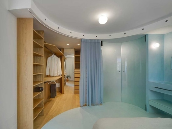 A curtain divider at the closet front and curved glass doors in the bathroom area follow the curved architectural element on the ceiling.