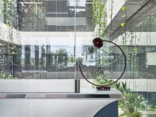 Copper-backed lightbulbs on black tracks illuminate the desk which sits in front of a foliage-rich concrete atrium (the architecture is by Elenberg Fraser).